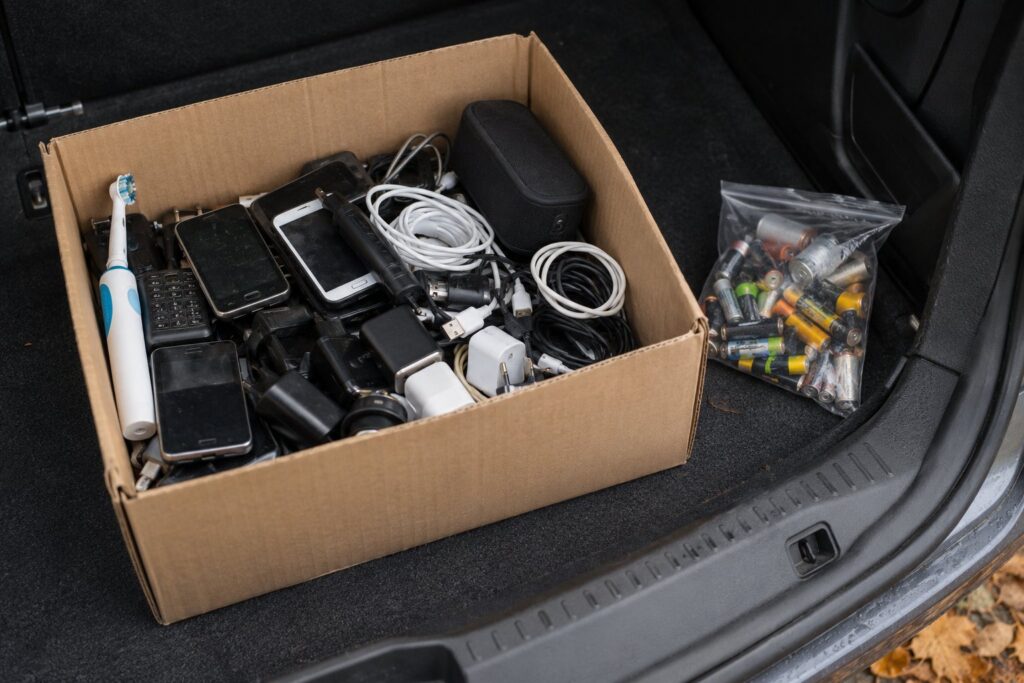 Papkasse med gamle mobiltelefoner, opladere, kabler og en elektrisk tandbørste sorteret til genbrugspladsen